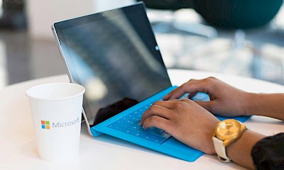 Person with blue laptop and Microsoft cup