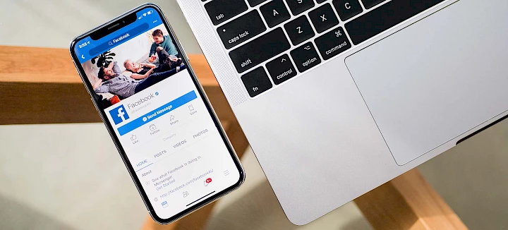 Smartphone mit geöffneter Facebook-Anwendung auf dem Display neben Laptop-Tastatur