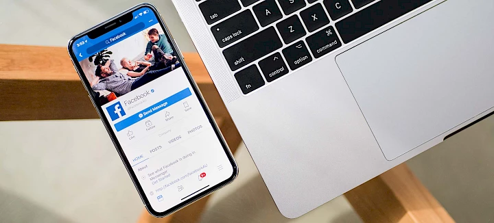Smartphone with Facebook application open on the display next to laptop keyboard