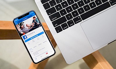 Smartphone mit geöffneter Facebook-Anwendung auf dem Display neben Laptop-Tastatur