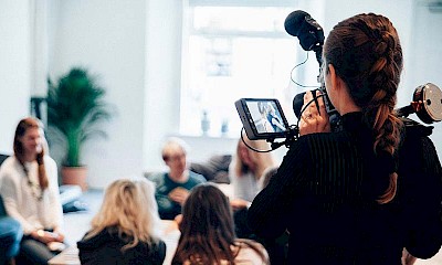 Kamerafrau während der Videoaufnahme von hinten zur Veranschaulichung von Pressemitteilungen