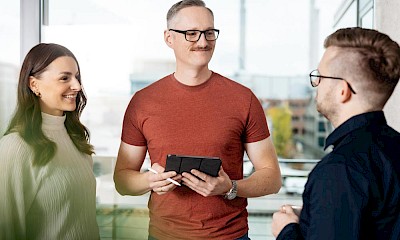 3 DREIKON employees talking, man in T-shirt in the centre holding a tablet