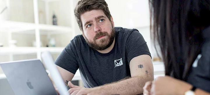 A man and a woman are sitting at a table looking at a laptop