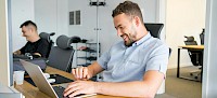 Ein Mann sitzt an einem Tisch und schaut auf einen Laptop