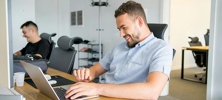 Ein Mann sitzt an einem Tisch und schaut auf einen Laptop