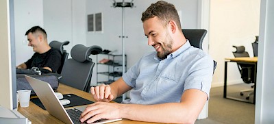 Mann sitzt am Schreibtisch und schaut auf Laptop