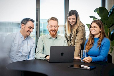 Zwei Männer und zwei Frauen sitzen am Tisch und schauen auf einen Laptop