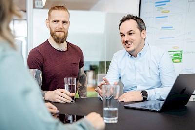 Two men talking in an agency, target group analysis in the background