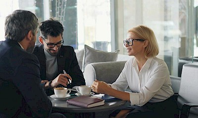 Zwei Männer und eine Frau sitzen an einem Tisch und unterhalten sich