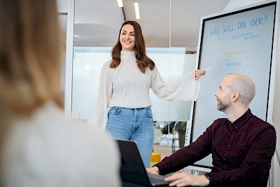 Een medewerkster van DREIKON staat bij het whiteboard en legt de zoekintentie van een gebruiker uit