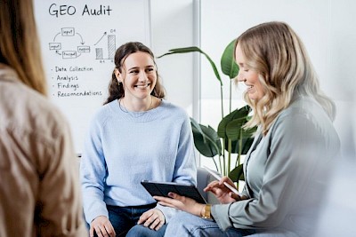 Two staff members are discussing AI in front of a whiteboard with GEO Audit